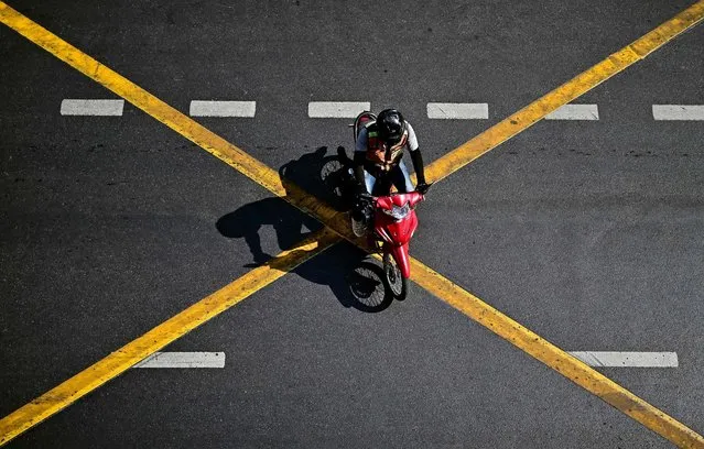 A motorcycle-taxi rider crosses a road in Bangkok on February 28, 2024. (Photo by Manan Vatsyayana/AFP Photo)