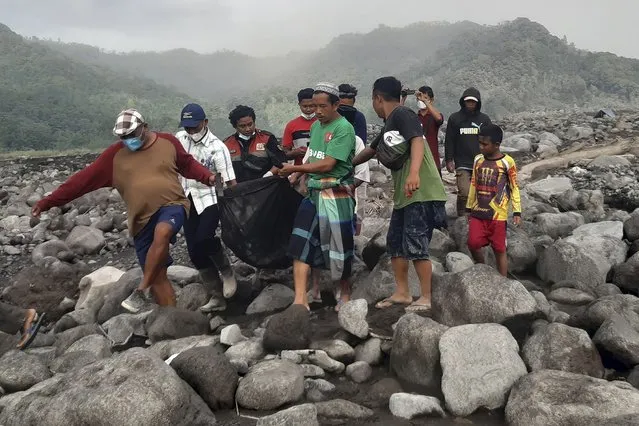 Rescuers and villagers carry a body bag containing the remains of a victim in the eruption of Mount Semeru, in Candi Puro village, Lumajang, East Java, Indonesia, Tuesday, December 7, 2021. (Photo by Rokhmad/AP Photo)