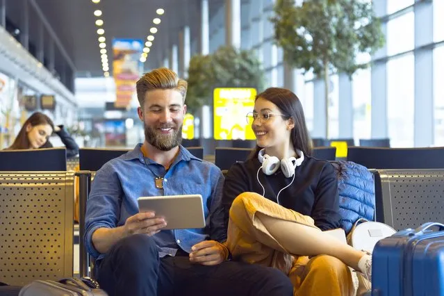 Young woman and man traveling by plane, using a digital tablet in airport waiting area. (Photo by izusek/Getty Images)