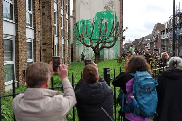 Crowds gather to view a Banksy artwork, a stencil of a person having spray painted tree foliage onto a wall behind a leafless tree, a graffiti artwork confirmed as being the work of the famous street artist near Finsbury Park in north London on March 18, 2024. (Photo by Adrian Dennis/AFP Photo)