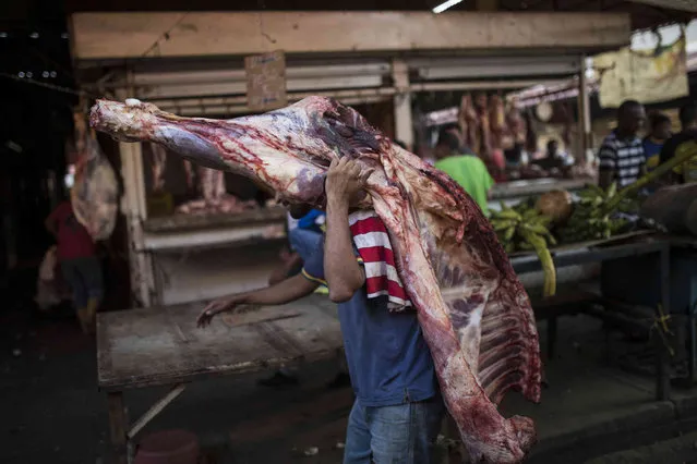 A vendor carries beef to a butcher shop at the flea market in Maracaibo, Venezuela, May 16, 2019. He'll have to sell it quickly, since perishables go bad quickly without refrigeration in Maracaibo's suffocating temperatures. (Photo by Rodrigo Abd/AP Photo)