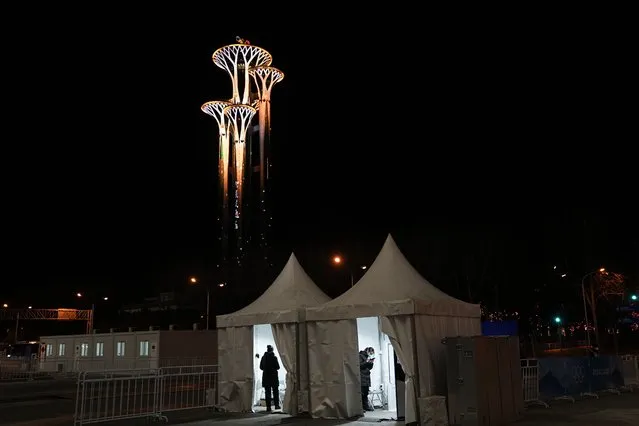 Two Olympic workers stand in their tents with the Beijing Olympic Tower in the background on the eve of the Chinese New Year ahead of the 2022 Winter Olympics, Monday, January 31, 2022, in Beijing. (Photo by Jae C. Hong/AP Photo)