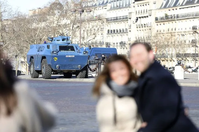 People pose in front of a police armored vehicle near at the Arc de Triomphe, Saturday, February 12, 2022 in Paris. Protesters angry over pandemic restrictions are driving toward Paris to blockade the French capital despite a police ban. The protesters organized online, galvanized in part by truckers who have blockaded Canada's capital. Paris region authorities deployed more than 7,000 police officers to tollbooths and other key sites to try to prevent a blockade. (Photo by Adrienne Surprenant/AP Photo)