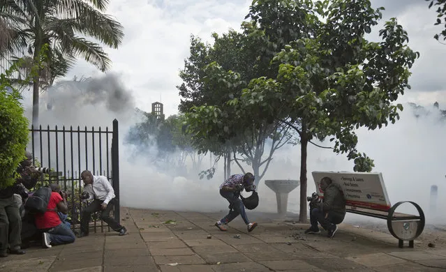 Kenyan photographers take cover from rocks thrown by protesters and tear gas fired by riot police, during a demonstration in downtown Nairobi, Kenya Monday, May 9, 2016. (Photo by Ben Curtis/AP Photo)