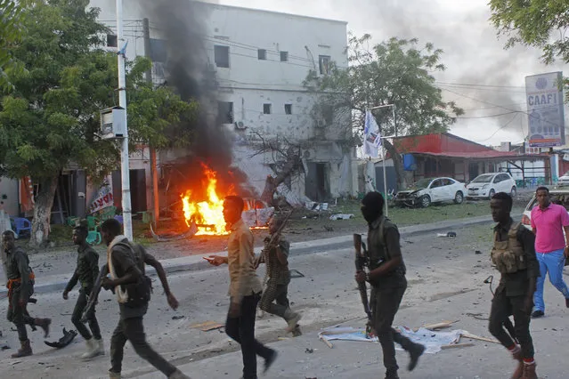 Somali security walk near a burning car after a car bomb attack on a restaurant in Mogadishu, Somalia Monday, May, 8, 2017. A Somali police officer said the car bomb exploded at a restaurant cafe in Somalia's capital Mogadishu, Monday, leaving many dead and injured.  (Photo by Farah Abdi Warsameh/AP Photo)