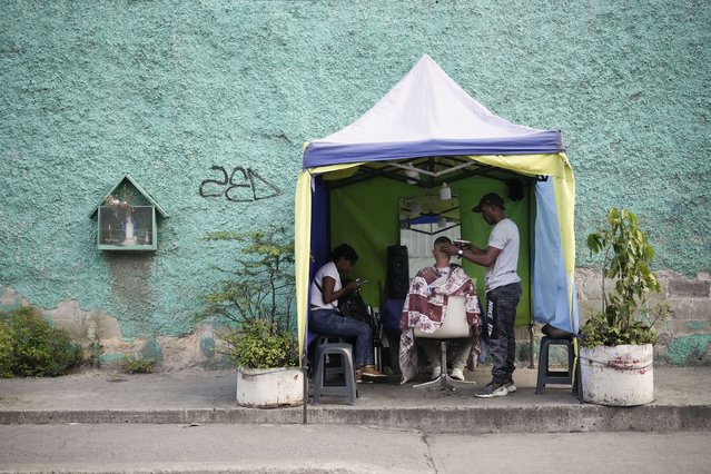 Luis Gragirena cuts a customer's hair in his makeshift salon, set up on a sidewalk in Caracas, Venezuela, July 23, 2024. (Photo by Fernando Vergara/AP Photo)