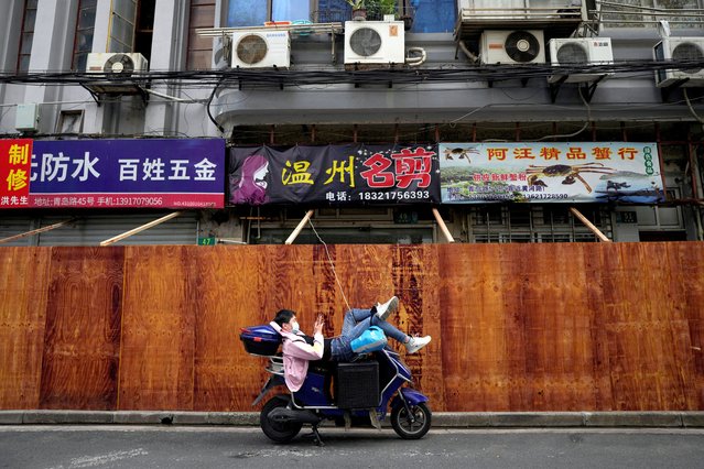 A man uses a mobile phone while leaning on a scooter in front of barricades of a sealed-off area, following the coronavirus disease (COVID-19) outbreak in Shanghai, China on March 30, 2022. (Photo by Aly Song/Reuters)