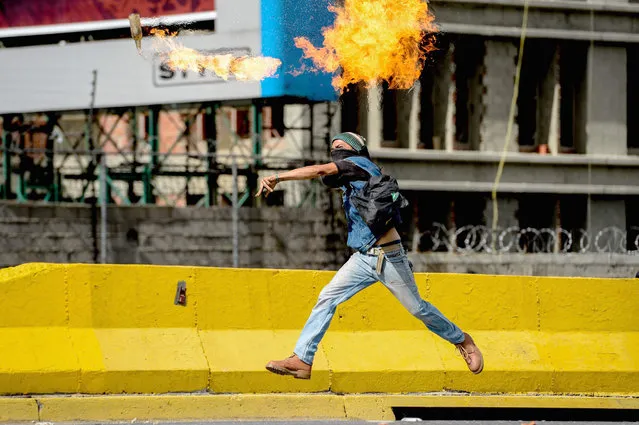 An opposition activist throws a molotov cocktail at the police during clashes that erupted in a march against Venezuelan President Nicolas Maduro held on May Day, in Caracas on May 1, 2017. Venezuela's beleaguered President Nicolas Maduro on Monday called for a new constitution, to be written by a “people's” body circumventing the opposition-held Congress. The decree was to “block the fascist coup” threatening the country, he told thousands of supporters in Caracas at a May Day rally. (Photo by Federico Parra/AFP Photo)