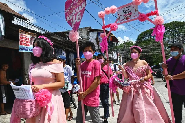 Supporters of vice president and presidential candidate Leni Robredo, wearing dresses to celebrate the Flores de Mayo (Flowers of May) religious festival, hand out leaflets during campaigning in a residential neighbourhood in Quezon City, suburban Manila on May 5, 2022. (Photo by Chaideer Mahyuddin/AFP Photo)