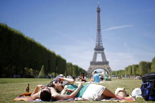 Tourists relax on the grass of the Champ de Mars in front of the Eiffel Tower in Paris, France, August 2, 2015 as warm summer temperatures return to the French capital. France has been the world's most visited country since the 1980's, welcoming 84 million tourists last year. (Photo by Stephane Mahe/Reuters)