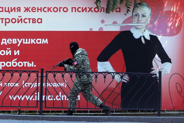 A pro-Russian fighter runs past a huge poster during fighting near a regional police department in downtown Donetsk, eastern Ukraine, Tuesday, July 1, 2014. Ukraine renewed its attacks against armed pro-Russian separatists Tuesday after the president called off a unilateral cease-fire, carrying out air and artillery strikes against rebel positions in eastern Ukraine. (Photo by Dmitry Lovetsky/AP Photo)