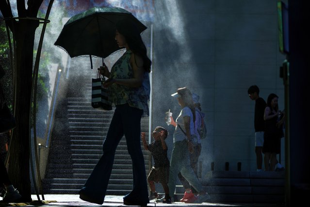 Shoppers walk by as a child plays near a mist machine at an outdoor shopping mall in Beijing, Monday, August 12, 2024. (Photo by Andy Wong/AP Photo)