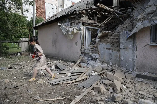A girl carries a dog as she walks past a house damaged from shelling in the Leninsky district of Donetsk, on the territory which is under the Government of the Donetsk People's Republic control, eastern Ukraine, Monday, June 6, 2022. (Photo by Alexei Alexandrov/AP Photo)