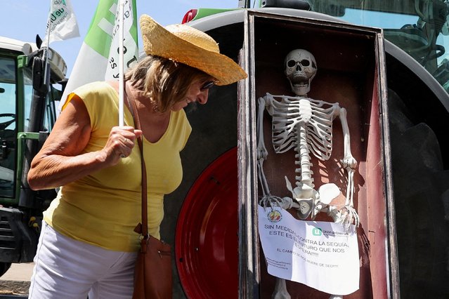 A woman looks at a paper and a skeleton figure which are placed next to a tractor as farmers protest over effects of drought and demand action from the government, in Madrid, Spain on July 5, 2023. (Photo by Violeta Santos Moura/Reuters)