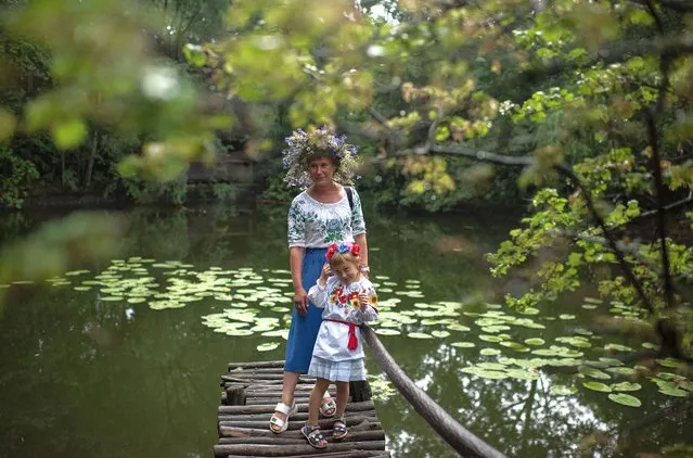 A woman wearing a traditional Ukrainian costume and her daughter pose for a portrait during the Ivana-Kupala celebration in Mamayeva Sloboda open air museum on July 6, 2022 in Kyiv, Ukraine. Kupala Night, also known as Ivana-Kupala, is a midsummer holiday in many slavic countries. Among the common rituals, women may float wreaths down a river to divine their romantic fortune, and couples leap hand-in-hand over bonfires in a bid for future togetherness. (Photo by Alexey Furman/Getty Images)