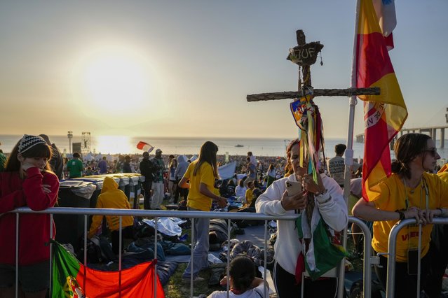 Pilgrims wake up after sleeping at the Parque Tejo in Lisbon where Pope Francis will preside over a mass celebrating the 37th World Youth Day, Sunday, August 6, 2023. An estimated 1.5 million young people filled the parque on Saturday for Pope Francis' World Youth Day vigil, braving scorching heat to secure a spot for the evening prayer and to camp out overnight for his final farewell Mass on Sunday morning. (Photo by Gregorio Borgia/AP Photo)