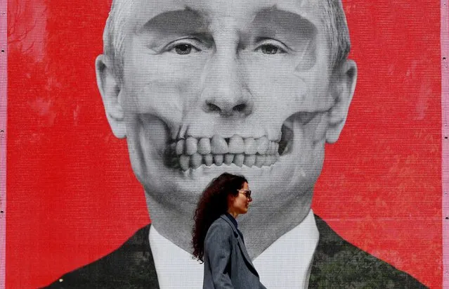 A Romanian woman passes by in front a printed mesh depicting Russian President Vladimir Putin, part of a anti-war art exhibition  in the King's Square, located near the Russian Federation's embassy compound, in Bucharest, Romania, where it was launched on 29 April 2022. “Special Artistic Operation” is the name of the street art exhibition with works by Ukrainian and Romanian artists near the Russian Embassy in Bucharest. (Photo by Robert Ghement/EPA/EFE)