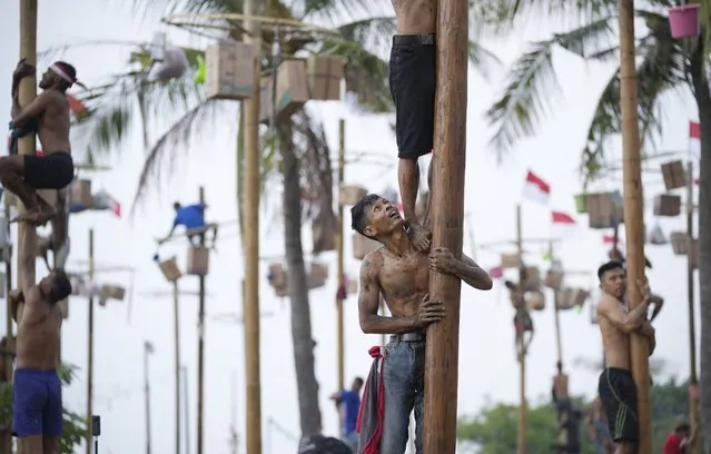 Participants try to reach the prizes during a greased-pole climbing competition held as a part of Independence Day celebrations at Ancol Beach in Jakarta, Indonesia Wednesday, August 17, 2022. Indonesia is celebrating its 77th anniversary of independence from the Dutch colonial rule. (Photo by Tatan Syuflana/AP Photo)