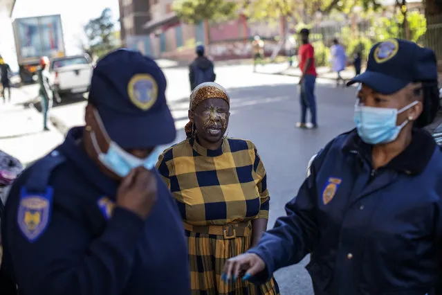 A woman (C) reacts in pain after being sprayed with pepper spray by a member of the South African Police Service (SAPS) (not visible) for not wearing a face mask in public, in Hillbrow, Johannesburg, on May 1, 2020, as members of the Johannesburg Metro Police Department (JMPD) walk away. South Africa began to gradually loosen its strict COVID-19 coronavirus lockdown on May 1, 2020, after five weeks of restrictions. Social distancing and wearing masks in public and at workplaces will be mandatory. (Photo by Michele Spatari/AFP Photo)
