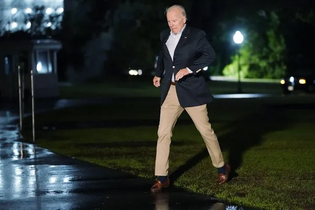 President Joe Biden navigates the muddy grass on a rainy night as he walks from Marine One on the South Lawn of the White House in Washington, late Monday, October 3, 2022. He and first lady Jill Biden were returning from a trip to Puerto Rico to survey hurricane damage. (Photo by Susan Walsh/AP Photo)