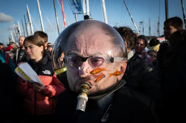 A man wearing an aquarium with goldfishes on his head walks among the pedestrians at the “Village de Saint-Malo”, the start point of the Route du Rhum solo sailing race, in Saint-Malo on November 1, 2022. The Route du Rhum solo sailing race starts on November 6, 2022, from Saint-Malo to  Pointe-a-Pitre in Guadeloupe. (Photo by Loic Venance/AFP Photo)