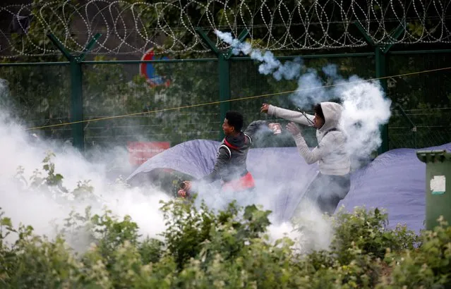 Migrants throw objects at French police officers in a cloud of tear gas as police dismantle a makeshift shelter camp in Calais, France on July 10, 2020. (Photo by Pascal Rossignol/Reuters)