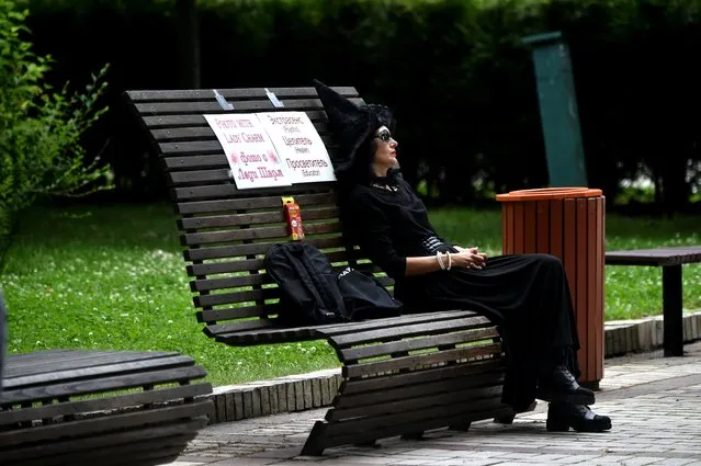 A woman dressed as a witch dozes in the absence of clients as she sits on a bench with a placard reading “Photo with lady Charm. Psychic. Healer. Educator” in the center of the Ukrainian capital of Kiev on July 13, 2020. (Photo by Sergei Supinsky/AFP Photo)