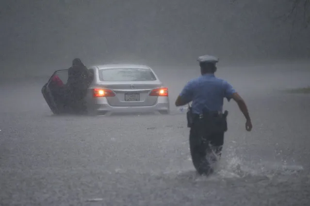 A Philadelphia police officer rushes to help a stranded motorist during Tropical Storm Isaias, Tuesday, August 4, 2020, in Philadelphia. The storm spawned tornadoes and dumped rain during an inland march up the U.S. East Coast after making landfall as a hurricane along the North Carolina coast. (Photo by Matt Slocum/AP Photo)