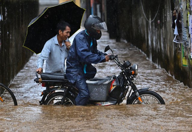 A pillion rider pushes a moped through a flooded street after heavy rainfall in Guwahati on April 28, 2025. (Photo by Biju Boro/AFP Photo)