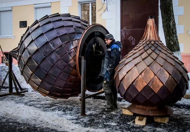 A worker stands next to two metal Russian traditional onion domes during the  renovation of a church in the historical center of Yaroslavl on January 24, 2018. (Photo by Mladen Antonov/AFP Photo)
