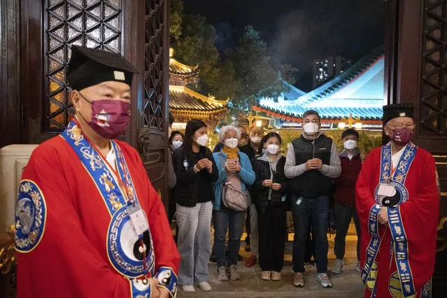 Taoists wearing face masks stand as masked worshippers wait to burn their first joss sticks at the Wong Tai Sin Temple, Saturday, January 21, 2023, in Hong Kong, to celebrate the Lunar New Year which marks the Year of the Rabbit in the Chinese zodiac. (Photo by Bertha Wang/AP Photo)