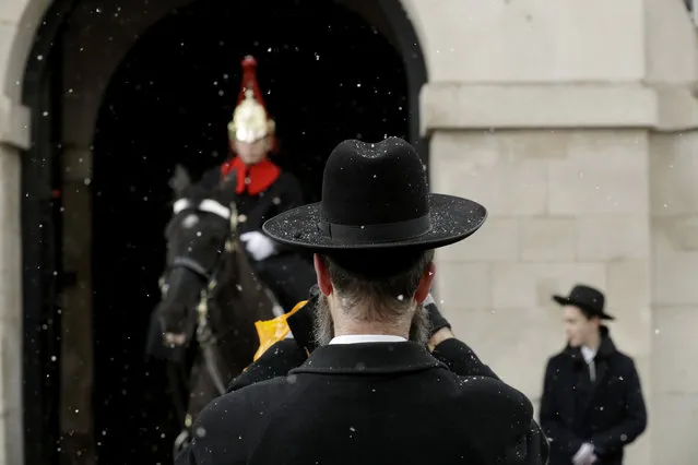 Tourists take pictures as a flurry of snow falls on a member of the Queen's Life Guard and his horse, guarding their ceremonial position outside Horse Guards during a sporadic snow shower in London, Monday, February 26, 2018. (Photo by Matt Dunham/AP Photo)