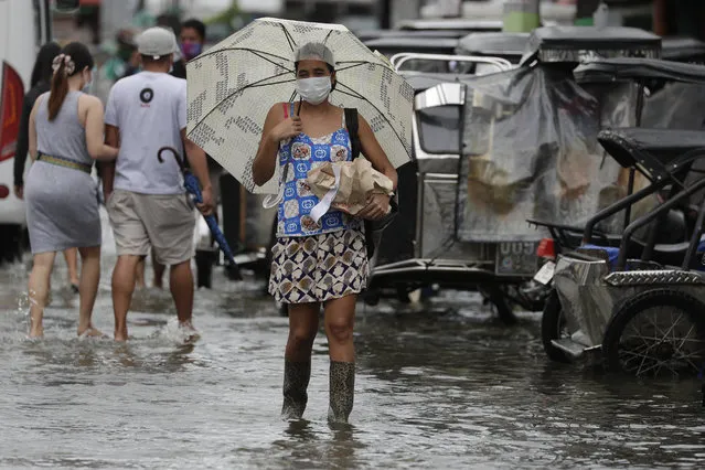 A woman wearing masks to prevent the spread of the coronavirus carries items as she wades along a flooded road due to Typhoon Molave in Pampanga province, northern Philippines on Monday, October 26, 2020. (Photo by Aaron Favila/AP Photo)