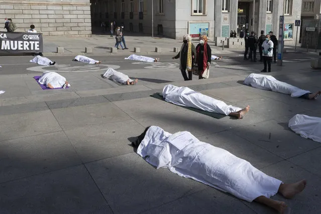 Two women walk past activists from Extinction Rebellion lying down outside the Spanish parliament during a protest with symbolic corpses coinciding with All Saints' Day, also known as Day of the Dead, Madrid, Spain, Sunday, November 1, 2020. The protest is to call attention to the causes of death related to the climate crisis. Part of the banner reads “Death”. (Photo by Paul White/AP Photo)
