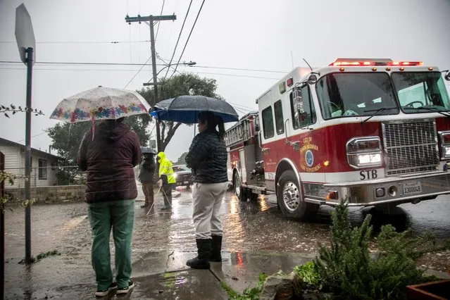 Residents stand near a fire truck on a flooded street in east Santa Barbara, California, January 9, 2023. (Photo by Erica Urech/Reuters)