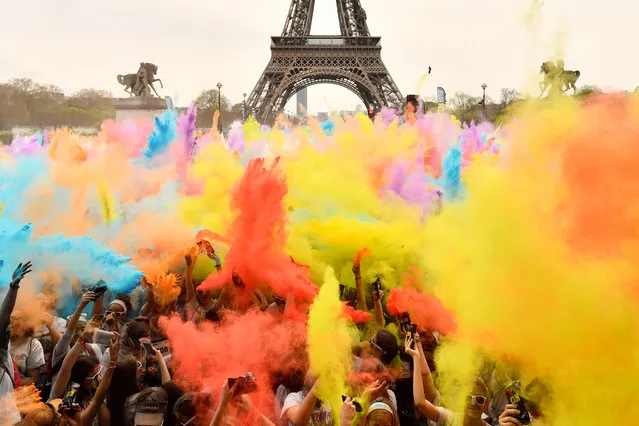People throw coloured powder as they celebrate finishing their five kilometers in the Color Run 2018 at the Eiffel Tower in Paris on April 15, 2018. Runners are showered with coloured powder at stations along the way in the five kilometres Color Run in which participant are all equal, no winners nor prizes for the finishers. (Photo by Christophe Simon/AFP Photo)