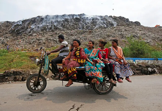 A man transports passengers on an improvised motor-rickshaw as they drive past a burning garbage dump site on the occasion of Earth Day, in Kolkata, India, April 22, 2018. (Photo by Rupak De Chowdhuri/Reuters)