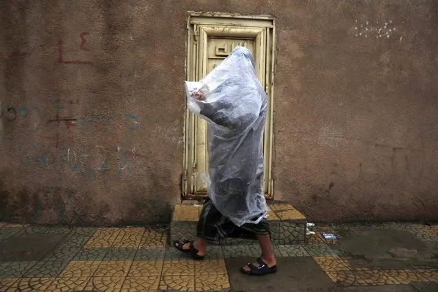 A man and his child wear a plastic poncho over their heads to protect them from the rain during heavy rainfall in Sana'a, Yemen, 13 April 2023. Torrential rains have caused floods in Sana'a and other areas of Yemen over the past few days. (Photo by Yahya Arhab/EPA)