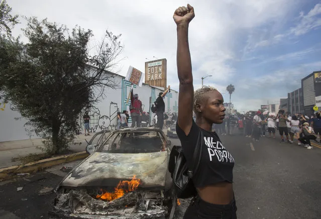 A protester poses for photos next to a burning police vehicle in Los Angeles, Saturday, May 30, 2020, during a demonstration over the death of George Floyd. a black man who was killed in police custody in Minneapolis on May 25. (Photo by Ringo H.W. Chiu/AP Photo)