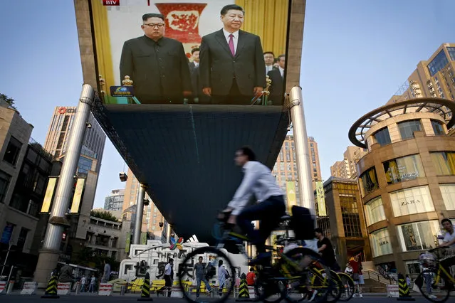 People bicycle past a giant TV screen broadcasting the meeting of North Korean leader Kim Jong Un and Chinese President Xi Jinping during a welcome ceremony at the Great Hall of the People in Beijing, Tuesday, June 19, 2018. Kim is making a two-day visit to Beijing starting Tuesday and is expected to discuss with Chinese leaders his next steps after his nuclear summit with U.S. President Donald Trump last week. (Photo by Andy Wong/AP Photo)