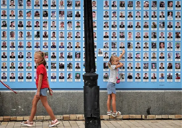 Girls play next to the memory wall of fallen defenders of the country, amid Russia's attack of Ukraine, in Kyiv, Ukraine on July 1,2023. (Photo by Gleb Garanich/Reuters)