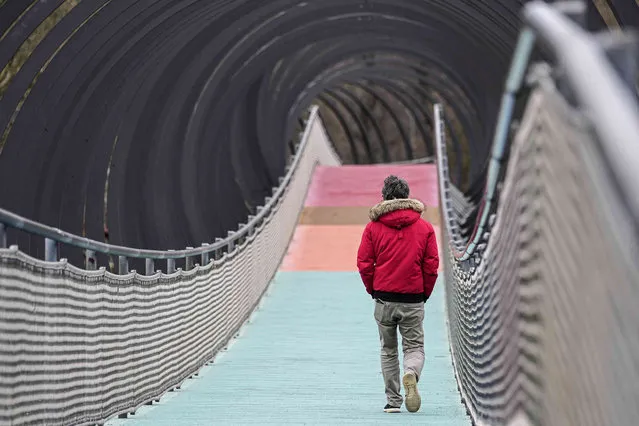 A man walks on a visually artful bridge over the canal in Oberhausen, western Germany, on a grey rainy Monday, March 20, 2023. (Photo by Martin Meissner/AP Photo)