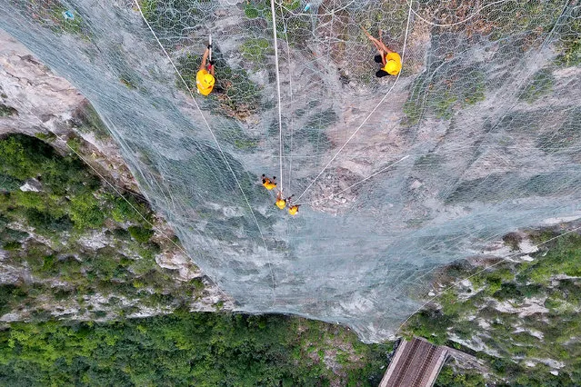 Staff members climb down a cliff to eliminate potential falling rocks above a tunnel of Houma-Yueshan Railway in central China's Henan Province, August 9, 2018. Railway maintenance workers work on the cliff to clear loose rocks above a rail tunnel here during flood season. (Photo by Li Jianan/Xinhua/Alamy Live News)