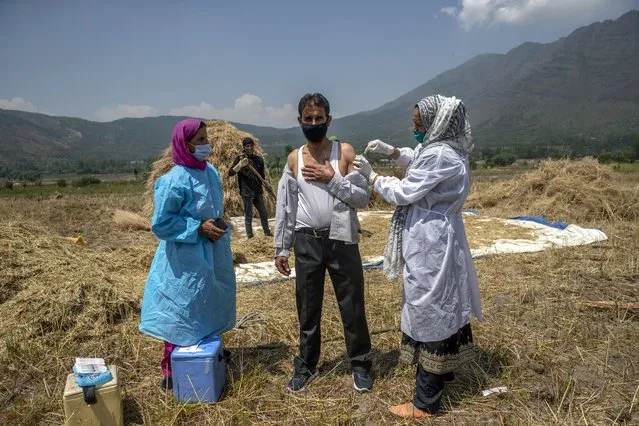 A health worker administers the AstraZeneca vaccine for COVID-19 in a paddy field in Tral village south of Srinagar, Indian controlled Kashmir, Saturday, June 5, 2021. (Photo by Dar Yasin/AP Photo)