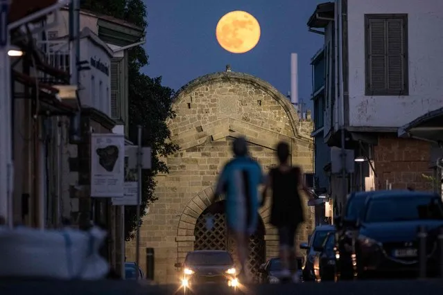People walk beneath the rising Strawberry super moon towards the Venetian-built Famagusta gate in the old walled city of Cyprus' capital Nicosia on June 24, 2021. Famagusta gate, one of the three main gates of the old city of Nicosia, was built in 1567 during the period of Venetian rule of the island of Cyprus. It was subsequently restored in 1821 during the reign of Ottoman Sultan Mahmud II, with the Sultan's seal (tugra) displayed atop its gatehouse. (Photo by Amir Makar/AFP Photo)