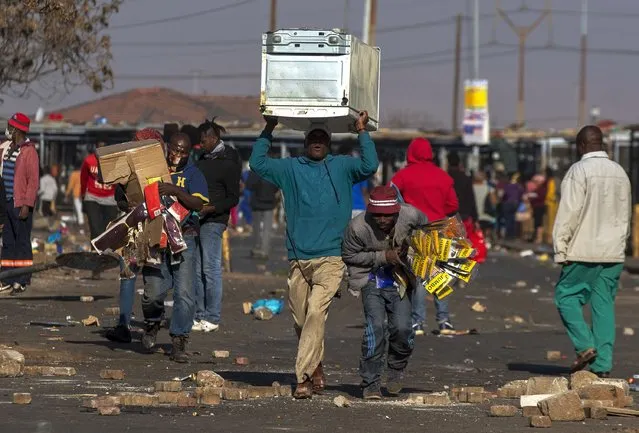 Looters carry items at Letsoho Shopping Centre in Katlehong, east of Johannesburg, South Africa, Monday, July 12, 2021. Police say six people are dead and more than 200 have been arrested amid escalating violence during rioting that broke out following the imprisonment of South Africa's former President Jacob Zuma. (Photo by Themba Hadebe/AP Photo)