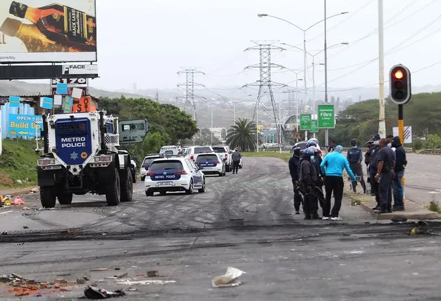 Police, on right, patrol a street in Durban, South Africa, Friday July 9, 2021, after protesters erected burning barricades to protest the imprisonment of former president Jacob Zuma. The Pietermaritzburg High Courtcourt has rejected Zuma's request to postpone his jail term of 15-months for contempt. (Photo by AP Photo/Stringer)