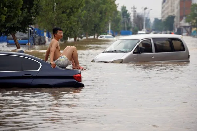 A man sits on a stranded vehicle on a flooded road following heavy rainfall in Zhengzhou, Henan province, China on July 22, 2021. (Photo by Aly Song/Reuters)