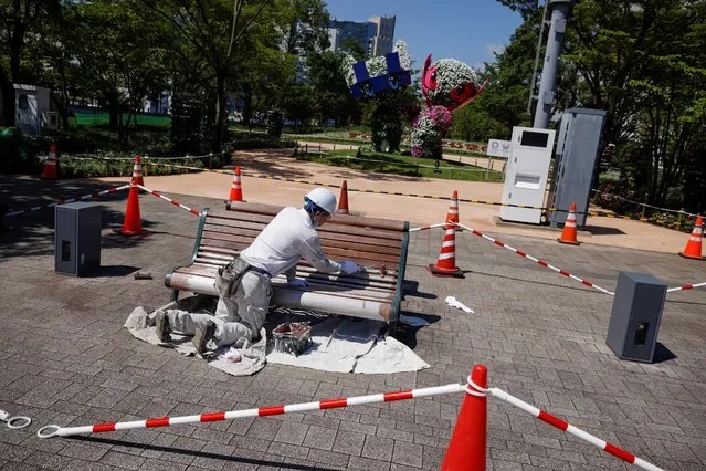 A worker paints a bench in front of the Tokyo 2020 Olympic and Paralympic mascots Miraitowa and Someity as the coronavirus disease (COVID-19) pandemic continues in Tokyo, Japan, July 17, 2021. (Photo by Thomas Peter/Reuters)