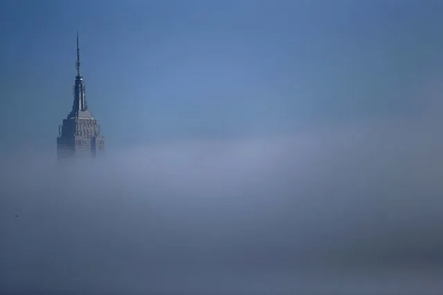 The tip of the Empire State Building peeks through thick fog seen from Pier A Park in Hoboken. (Photo by Julio Cortez/Associated Press)